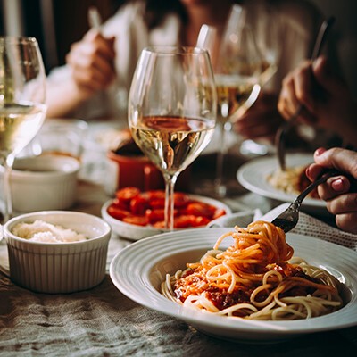 Mehrere Personen an einem Tisch mit Tellern voller Spaghetti und Weingläsern