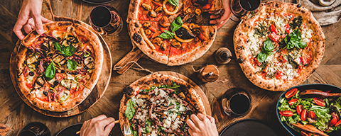 Mehrere verschiedene Pizzen auf einem Tisch an denen sich Leute bedienen - Rezeptbild aus der SPAR Mahlzeit