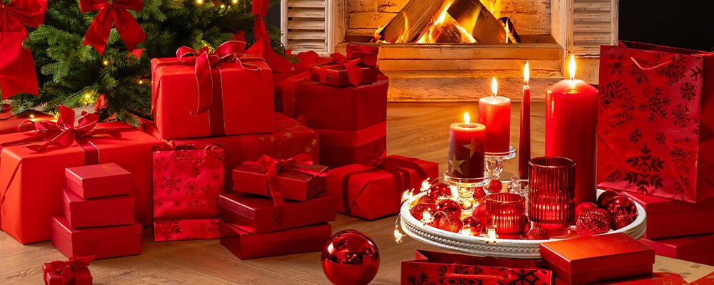 Ein weihnachtlich dekoriertes Zimmer mit Kamin, vor dem Geschenke liegen. Die Dekoration ist vorwiegend rot.