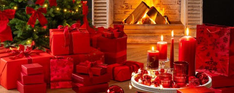 Ein weihnachtlich dekoriertes Zimmer mit Kamin, vor dem Geschenke liegen. Die Dekoration ist vorwiegend rot.