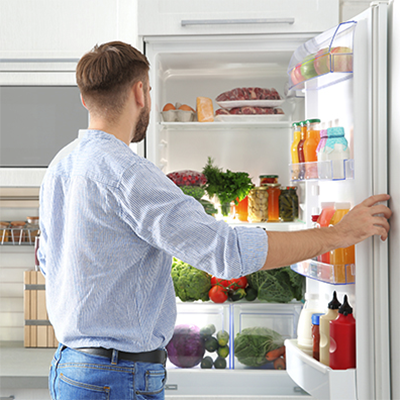 Ein Mann steht vor einem geöffneten Kühlschrank und schaut hinein