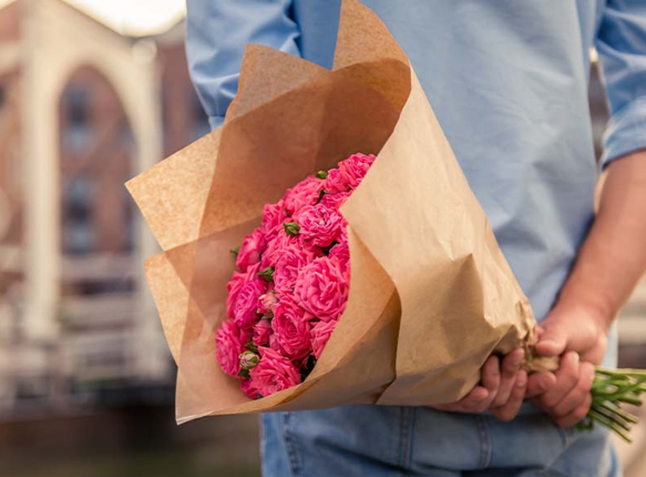 Ein Mann mit einem Strauß rosa Blumen hinter dem Rücken