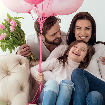 Ein Mann, eine Frau und ein kleines Mädchen mit Blumen und Ballons lachen
