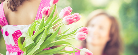 Ein kleines Mädchen mit einem Strauß rosa Tulpen hinter dem Rücken
