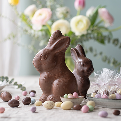 Zwei Osterhasen aus Schokolade auf einem Tisch mit vielen bunten Zuckereiern und mehr