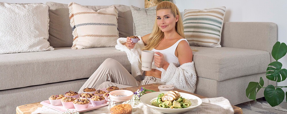 Pamela Reif sitzt neben frisch zubereitetem Essen und Produkten von Fackelmann neben einem Couchtisch