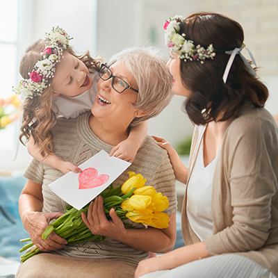 Eine Oma, ihre Tochter und ihre Enkelin mit Blumen beim Kuscheln