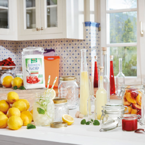 Mehrere Glasflaschen mit Säften, Früchte und Gläser auf einem Tisch