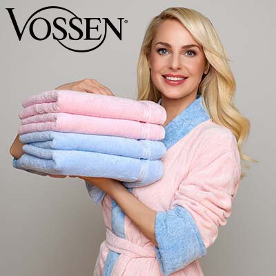 Silvia Schneider in einem blau-rosa Bademantel hält lächelnd einen Stapel blauer und rosafarbener Handtücher in den Händen