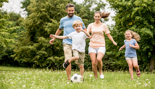 Eine Familie mit zwei Kindern beim Fußball spielen im Gras