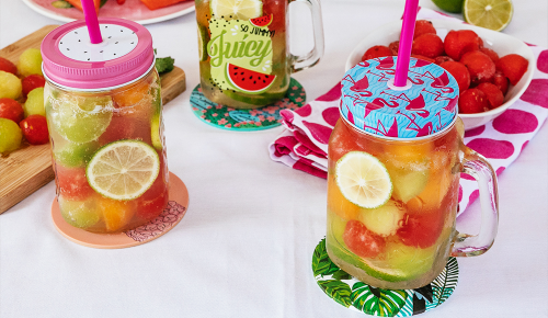 Zwei Schraubgläser mit bunten Deckeln gefüllt mit Obst, Beeren und Wasser