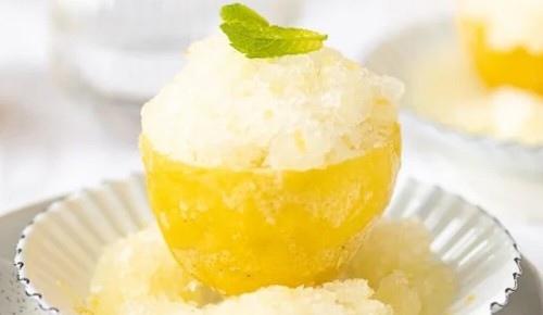 Zitronen Granita in Zitronenschale mit Minzblatt garniert.