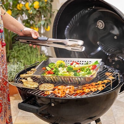 Eine Person an einem Grill mit Spießen, Gemüse und Fleisch