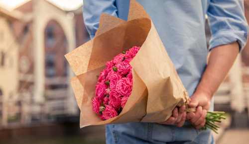 Eine Person hält einen großen Strauß pinker Blumen hinter dem Rücken