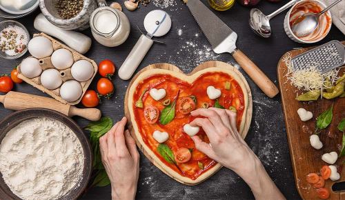 Eine Person beim Garnieren einer herzförmigen Pizza