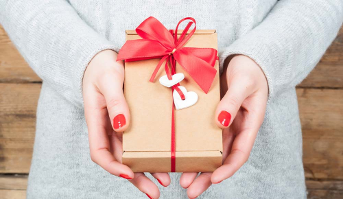 Eine Frau hält ein kleines Packerl mit einem roten Geschenkband in den Händen