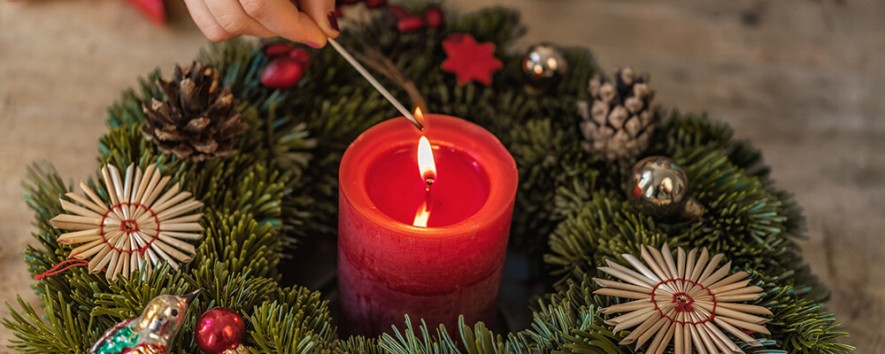 Eine Person zündet eine rote Kerze in einem Adventkranz an
