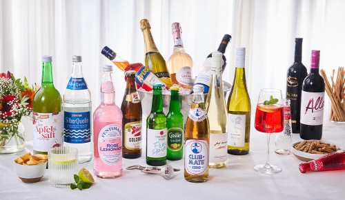 Auf einem Tisch mit einem weißen Tischtuch stehen verschiedenste Getränkeflaschen, Limonaden, Weine und Co.