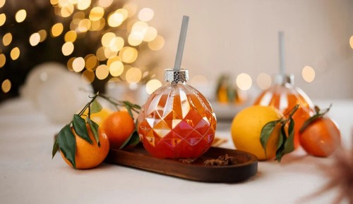 Ein Cocktailglas in Form einer Christbaumkugel voller orangem Aperol-Punsch auf einem festlich gedeckten, weißen Tisch