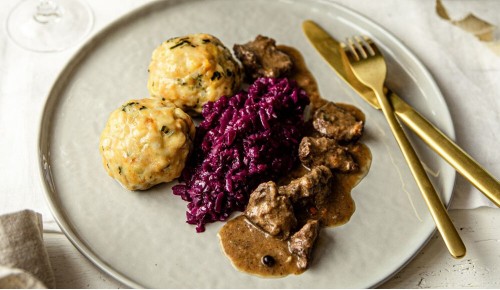 Hirschragout mit Knödel und Blaukraut schln angerichtet auf einem festlich gedeckten Tisch