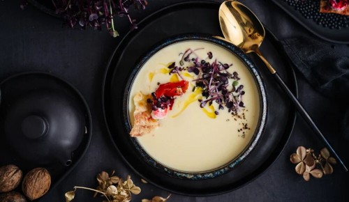 Eine Portion Rieslingsuppe mit Dekor aus Sprossen auf einem dunklen, festlich gedeckten Tisch
