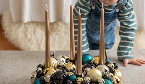 Ein kleines Kind schaut neugierig einen Adventkranz aus Chrisbaumkugeln an