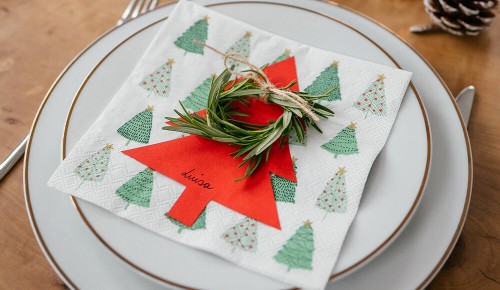 Eine Serviette mit Tannenbäumen, ein roter Papiertannenbaum und ein Rosmarinkranz