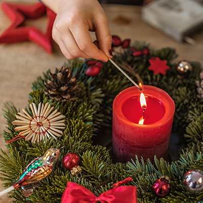 Eine Person zündet eine rote Kerze in einem Adventkranz an
