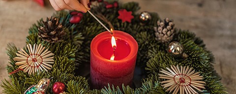 Eine Person zündet eine rote Kerze in einem Adventkranz an