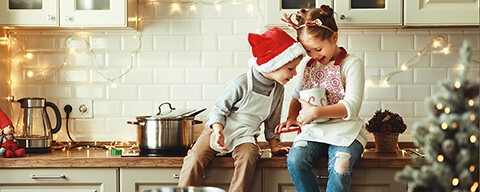 Zwei Kinder sitzen auf einer Küchenzeile und naschen Kekse