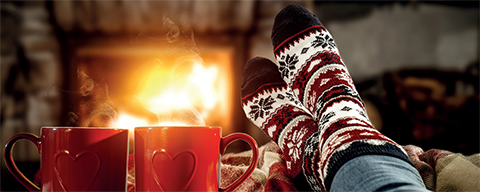 Eine Person sitzt mit Weihnachtssocken vor einem brennenden Kamin