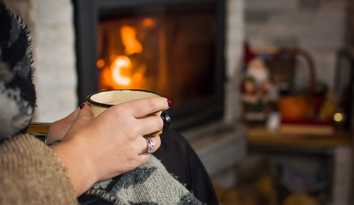 Eine Person mit einer Tasse Tee vor einem brennenden Kamin