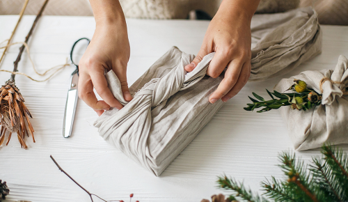 Zusammenknoten von Tuchenden eines Furoshiki-verpackten Geschenks