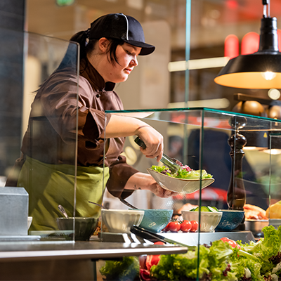 Eine Mitarbeiterin an einem Buffet eines INTERSPAR-Restaurants beim befüllen eines Salattellers