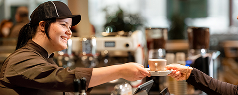 Eine Mitarbeiterin eines INTERSPAR-Restaurants beim Übergeben einer Tasse an eine Kundin