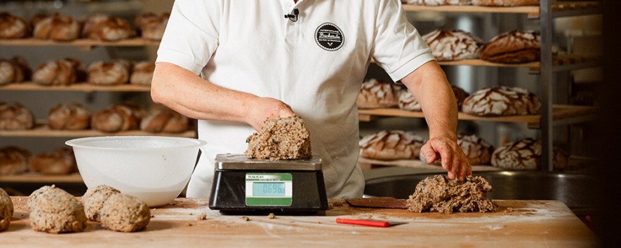 Ein/e Mitarbeiter:in beim Abwiegen von Teig für ein Brot
