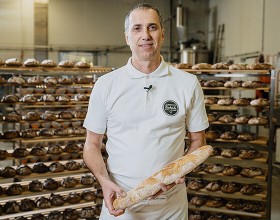 Der/die Backetubenleiter:in lächelt mit seinem/ihrem Bäckerliebling in der Hand in die Kamera