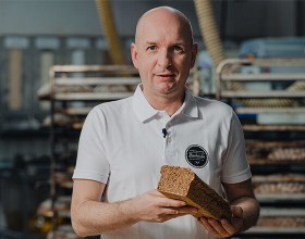 Der/die Backetubenleiter:in lächelt mit seinem/ihrem Bäckerliebling in der Hand in die Kamera