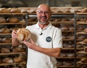 Der/die Backetubenleiter:in lächelt mit seinem/ihrem Bäckerliebling in der Hand in die Kamera