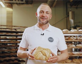 Der/die Backetubenleiter:in lächelt mit seinem/ihrem Bäckerliebling in der Hand in die Kamera