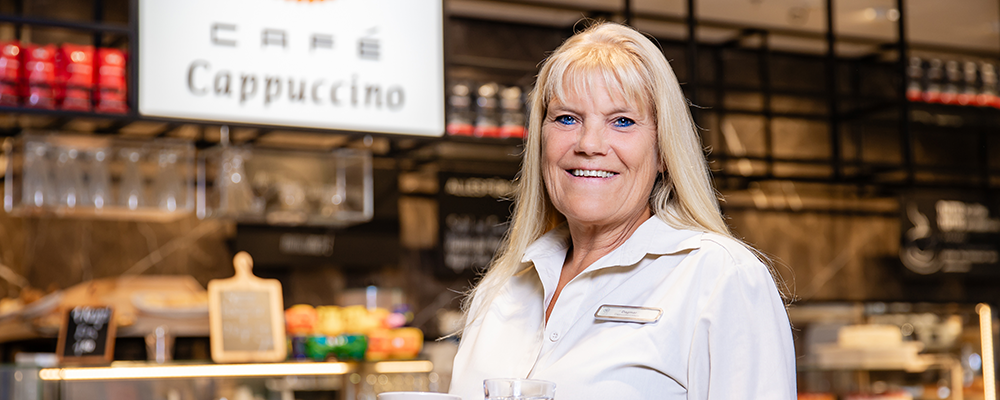 Eine Mitarbeiterin in einem Café Cappuccino lächelt in die Kamera