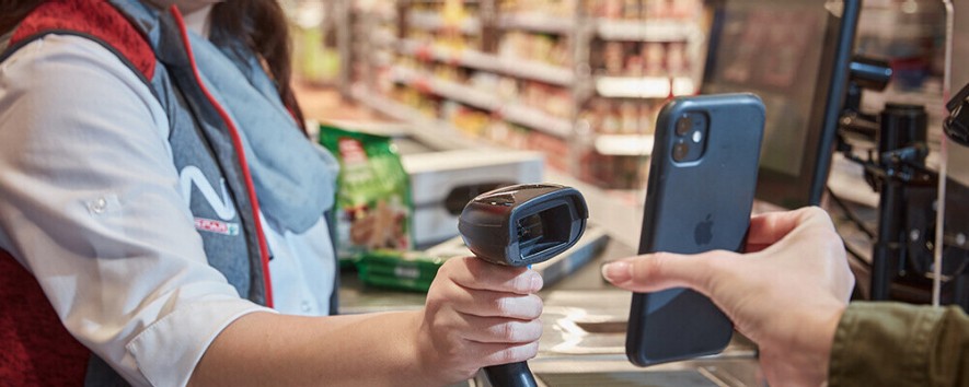Eine Mitarbeiterin scannt das Handy eines Kunden an einer INTERSPAR-Kassa