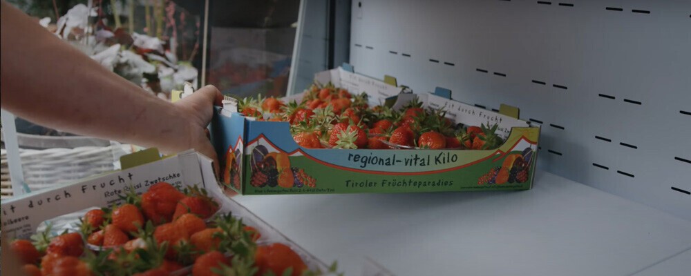 Eine Person stellt einen Karton mit Erdbeeren in ein Regal
