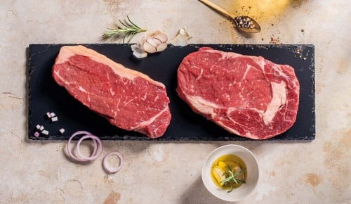 Zwei rohe Stücke Fleisch liegen auf einem schwarzen Schneidebrett
