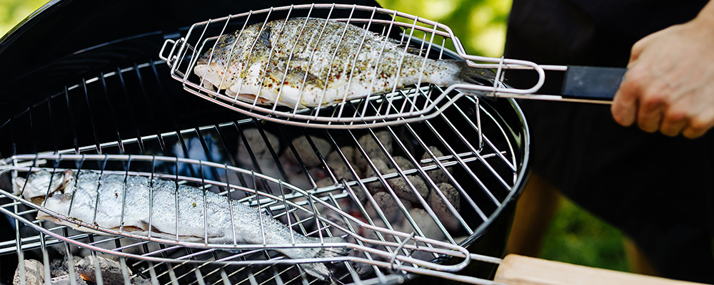 Fische in einer Grillzange auf einem Kugelgrill