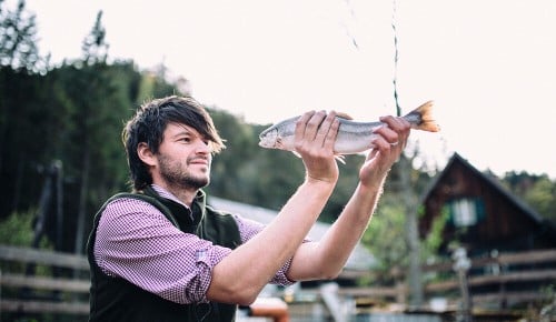 Ein Mitarbeiter von Michis Fischzucht mit einem Fisch in den Händen