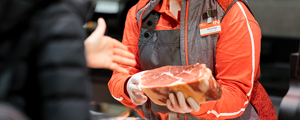 Ein/e INTERSPAR-Mitarbeiter:in mit einem Stück Schinken in der Hand