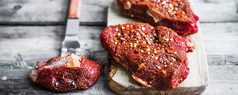 Drei marinierte Stücke Fleisch mit Gewürzen auf einem Brettchen
