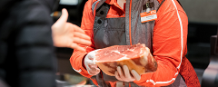 Ein/e INTERSPAR-Mitarbeiter:in mit einem Stück Schinken in der Hand