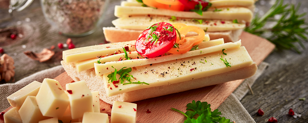 Ein aufgeschnittener Schnittkäse mit Tomaten und Kräutern auf einem Brot